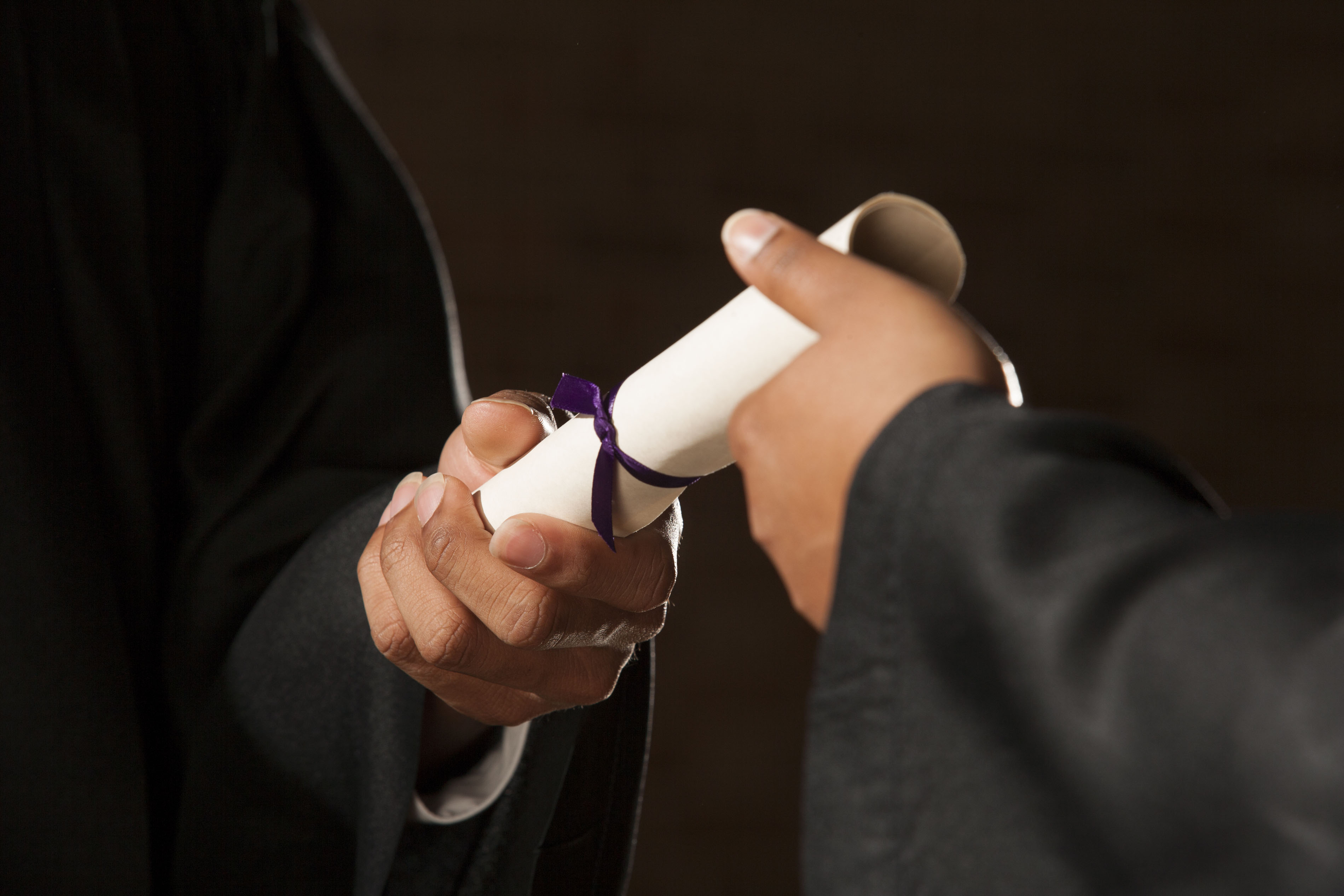 close up of student's hand being handed diploma at graduation ceremony
