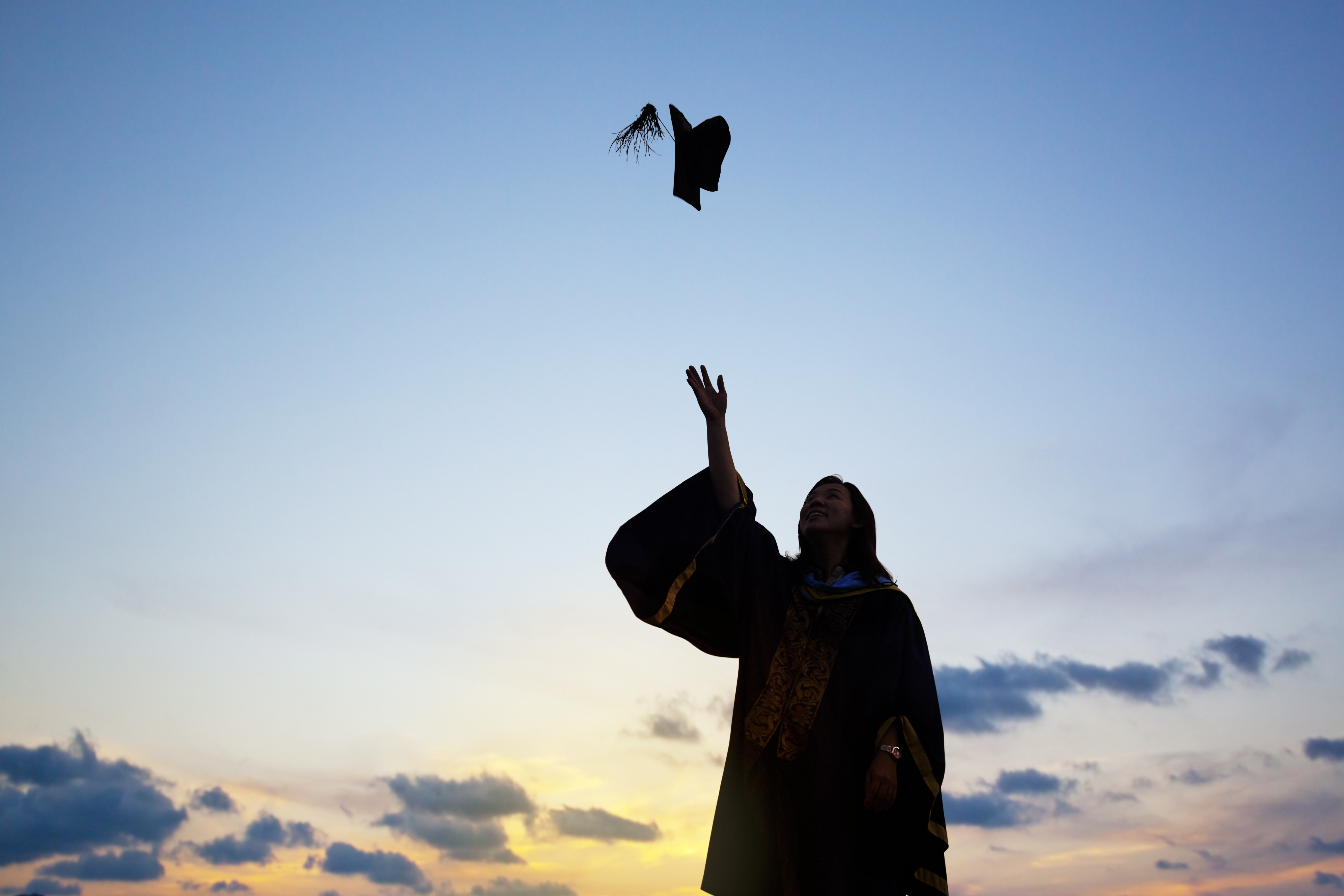 silhouette of young female student celebrating graduation by throwing her cap in the air